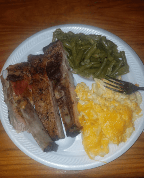 A plate with grilled ribs, green beans, and cheesy macaroni, served on a disposable white plate.