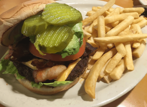 A juicy burger with bacon, cheese, lettuce, tomato, and pickles, served with a side of crispy French fries.