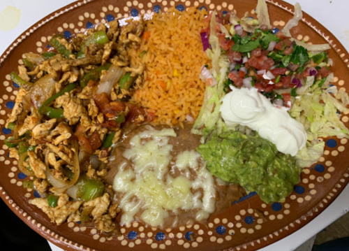 A colorful plate featuring chicken fajitas, rice, refried beans, guacamole, salad, and sour cream.