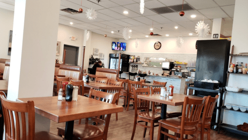 Interior of a cozy restaurant with wooden tables, chairs, and holiday decorations, featuring a counter and kitchen area.