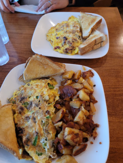 Two plates of breakfast: one with an omelet and toast, the other with an omelet, toast, and diced potatoes.