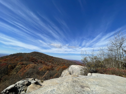 A panoramic view of a rocky landscape with autumn foliage under a bright blue sky with wispy clouds.