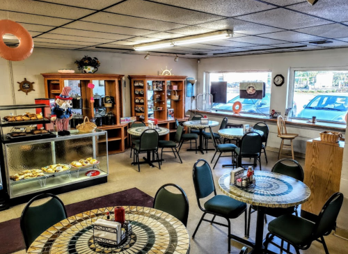 Cozy café interior with tables, chairs, a display case of pastries, and large windows letting in natural light.