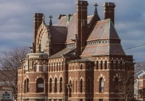 Historic brick building with ornate architecture, featuring multiple chimneys and decorative elements against a cloudy sky.