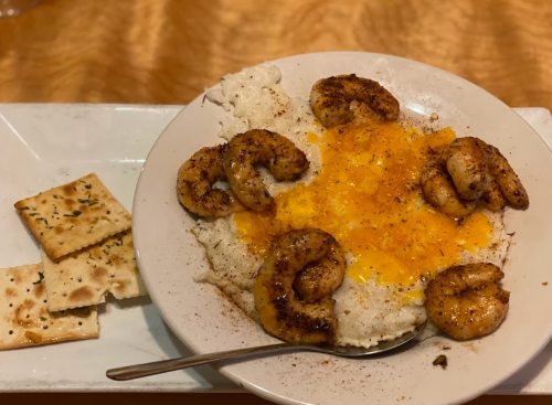 A plate of creamy grits topped with seasoned shrimp and shredded cheese, served with crackers on the side.