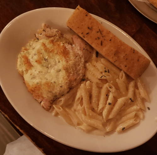 A plate of creamy pasta, baked chicken with a golden crust, and a slice of herb bread.