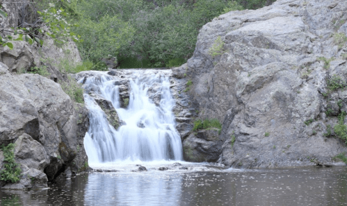 A serene waterfall cascades over rocks into a calm pool, surrounded by lush greenery.