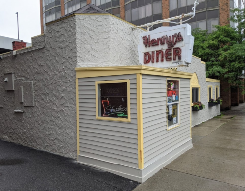 Exterior of Henry's Diner, featuring a vintage sign, gray textured walls, and colorful window decorations.