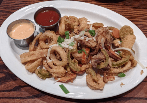 A platter of fried calamari and vegetables, served with two dipping sauces on the side.