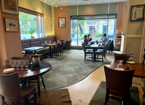 A cozy restaurant interior with tables set for dining, featuring a view of the street through large windows.