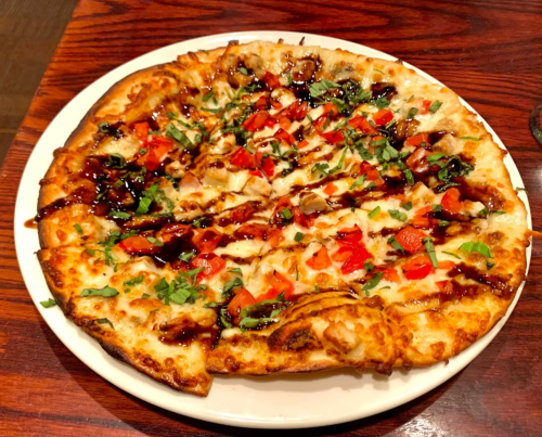 A pizza topped with diced tomatoes, herbs, and a drizzle of sauce on a golden crust, served on a white plate.