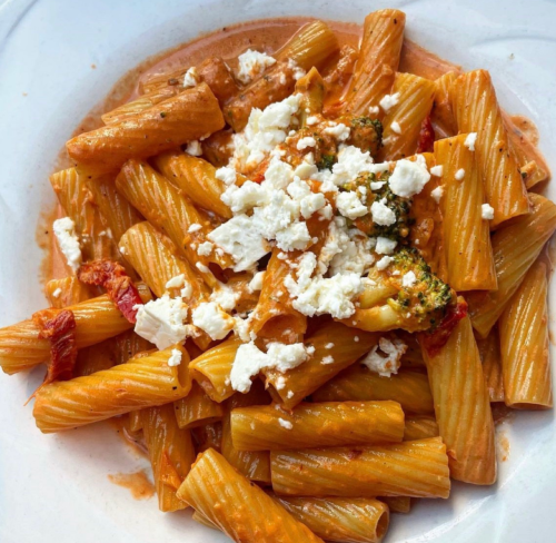 A plate of rigatoni pasta in a creamy tomato sauce, topped with crumbled feta cheese and pieces of broccoli.