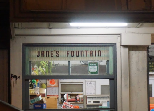 Sign above a window reads "Jane's Fountain," with a glimpse of items visible inside.