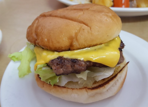 A close-up of a cheeseburger with lettuce on a toasted bun, featuring a melted slice of cheese on a beef patty.