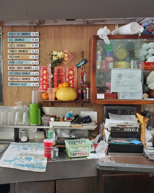 A cluttered counter with a menu board, food items, and various containers in a cozy eatery.