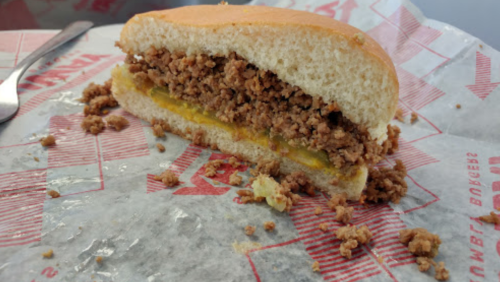 A partially eaten sandwich with a soft bun filled with seasoned ground meat and a layer of mustard.