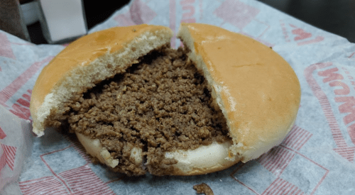 A split hamburger bun filled with seasoned ground beef, resting on a red and white paper wrapper.