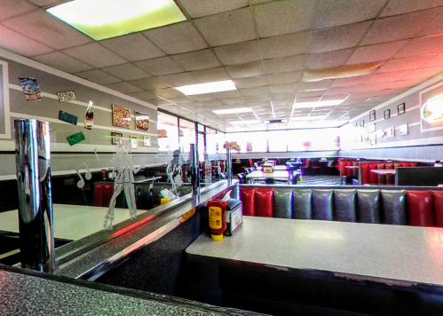A diner interior with red booths, a counter, and large windows letting in natural light. Decor includes vintage signs.
