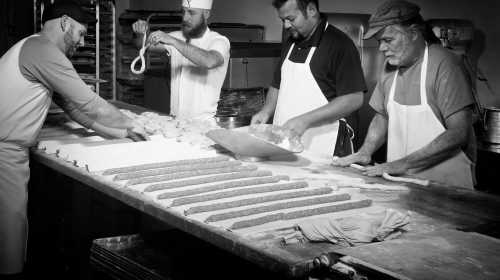 Four bakers working together in a bakery, shaping dough and preparing bread on a large wooden table.