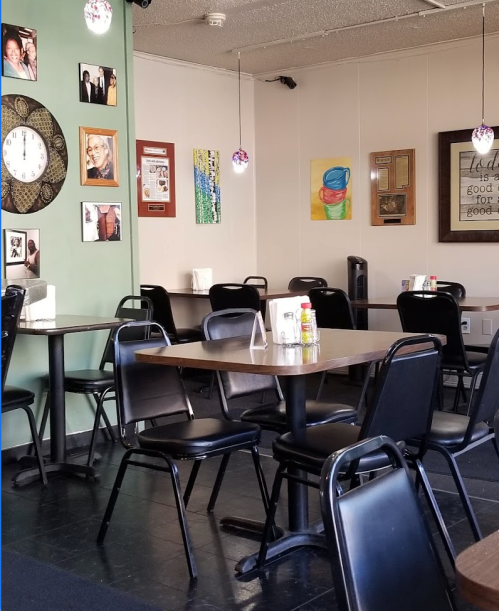 A cozy restaurant interior with black tables and chairs, colorful wall art, and decorative light fixtures.