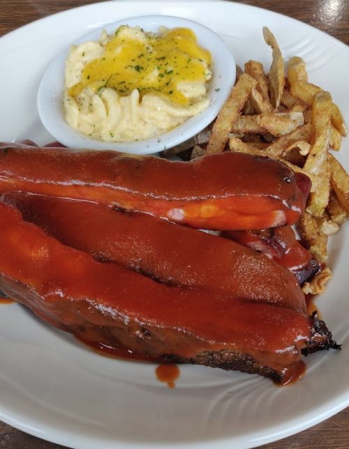A plate featuring three barbecue ribs with sauce, a side of mac and cheese, and crispy fries.