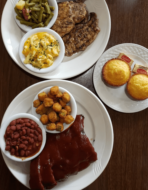 Two plates of Southern comfort food featuring meats, sides like green beans and cornbread muffins.