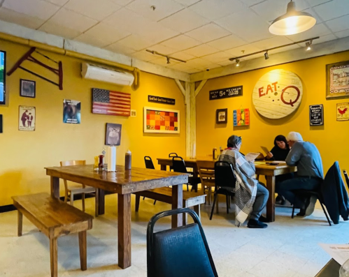 Cozy restaurant interior with wooden tables, wall art, and patrons dining together. Warm, inviting atmosphere.