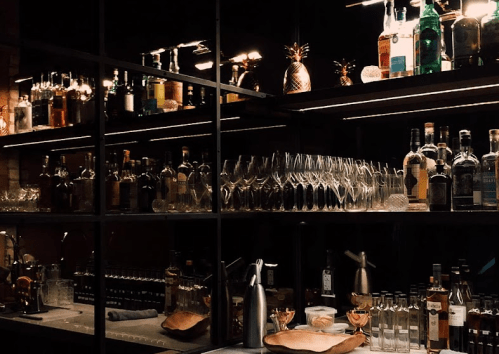 A dimly lit bar shelf displaying various bottles of liquor and glassware, creating an elegant atmosphere.