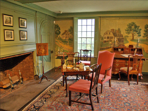 A cozy room with vintage furniture, a fireplace, and scenic wall murals depicting countryside landscapes.