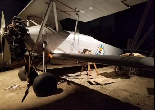 A vintage biplane displayed in a dimly lit museum, showcasing its propeller and distinctive wing design.