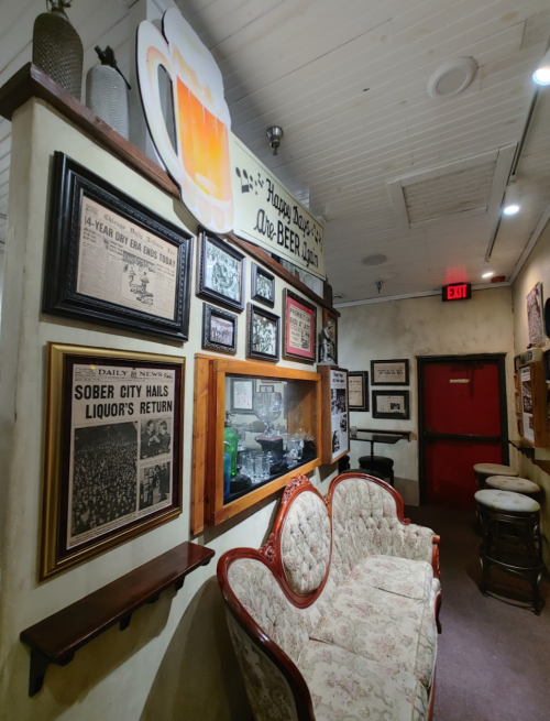 A cozy hallway in a bar, featuring vintage photos, a decorative beer sign, and a vintage couch.