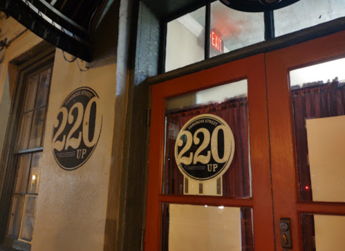 Exterior view of a restaurant entrance with a sign reading "220 Up" and a red door.
