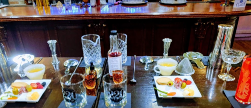 A bar setup with various cocktail ingredients, glasses, and garnishes on a wooden counter.