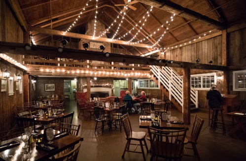 Cozy restaurant interior with wooden beams, string lights, and tables set for dining. A few patrons are seated.
