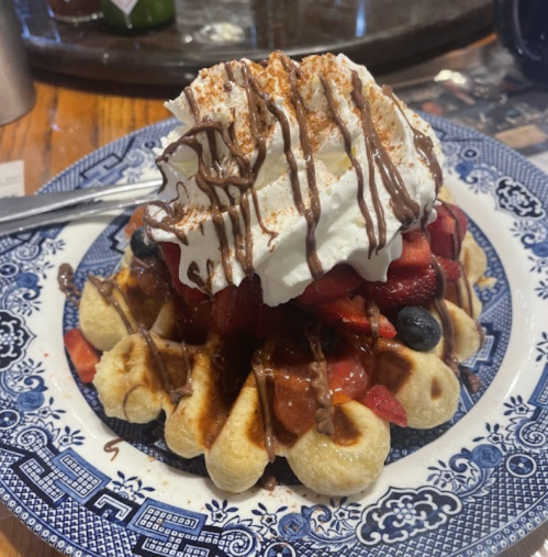 A plate of waffles topped with whipped cream, chocolate drizzle, and mixed berries.
