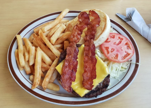 A plate with a cheeseburger topped with bacon, lettuce, and tomato, served with a side of French fries.