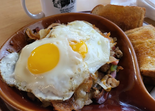 A hearty breakfast plate with two sunny-side-up eggs, sautéed vegetables, meat, and toast on the side.