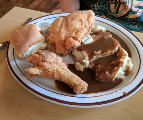 A plate of fried chicken, a bun, mashed potatoes with gravy, and a fried chicken leg on a wooden table.