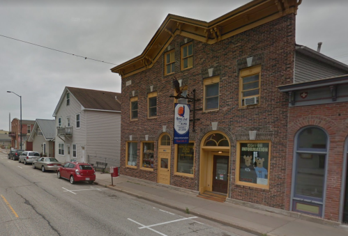A brick building with a sign for visitor information, surrounded by residential homes and parked cars on a cloudy day.