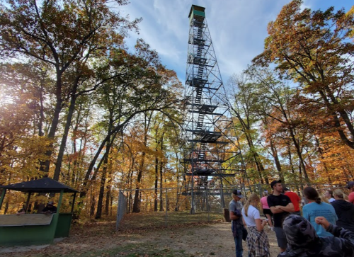 A tall observation tower surrounded by colorful autumn trees, with a group of people gathered nearby.