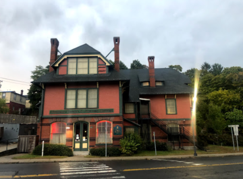 A large, red Victorian-style house with multiple chimneys and a staircase, set against a cloudy sky.