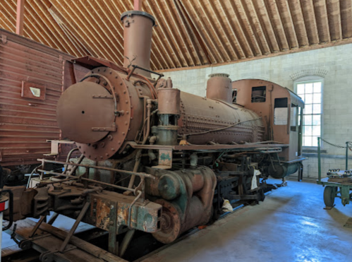 A vintage steam locomotive displayed indoors, showcasing its weathered exterior and intricate machinery.
