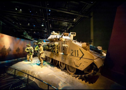 A military exhibit featuring a tank and soldiers in a museum setting, showcasing historical military equipment.