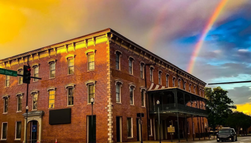 A brick building under a colorful sky with a rainbow, illuminated by sunset light, at a street intersection.