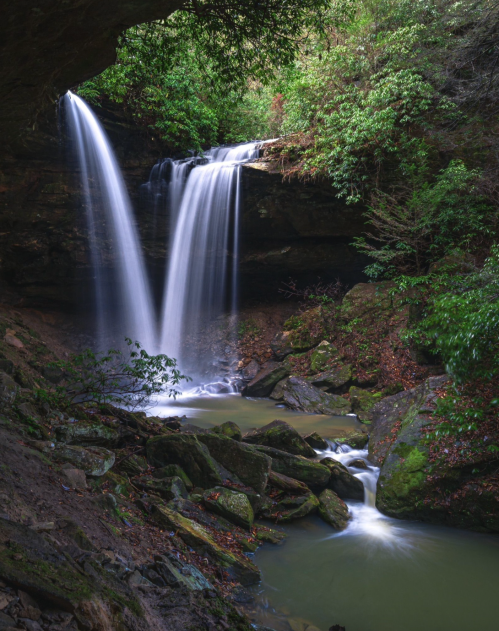 A serene waterfall cascades over rocks into a tranquil pool, surrounded by lush greenery and natural stone formations.