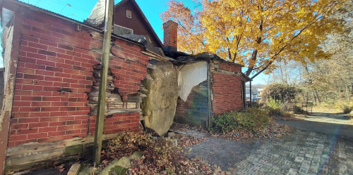 Abandoned brick building with crumbling walls, surrounded by autumn foliage and a clear blue sky.