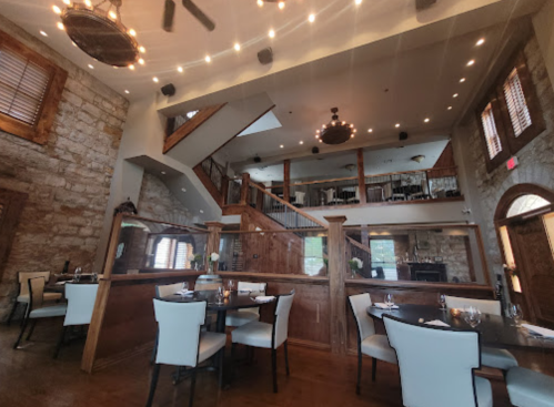 A spacious restaurant interior with wooden accents, elegant tables, and a two-level design featuring soft lighting.