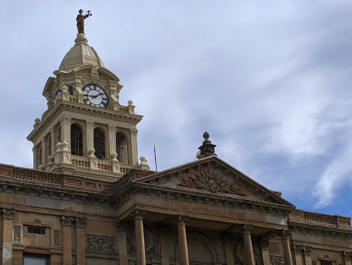 Historic building with a clock tower and a statue on top, under a cloudy sky.