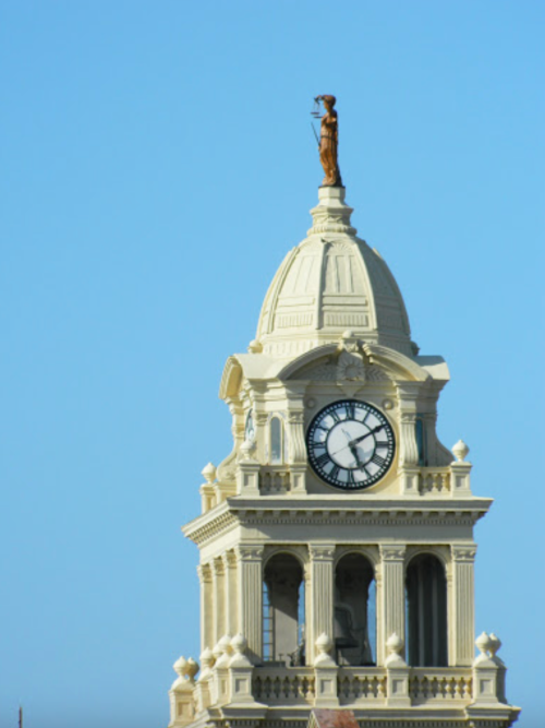 A clock tower topped with a statue of a woman holding scales, against a clear blue sky.