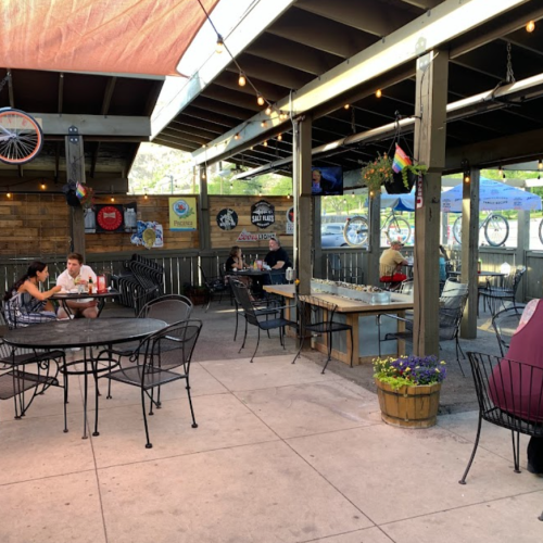 Outdoor dining area with tables and chairs, string lights, and patrons enjoying meals in a casual setting.